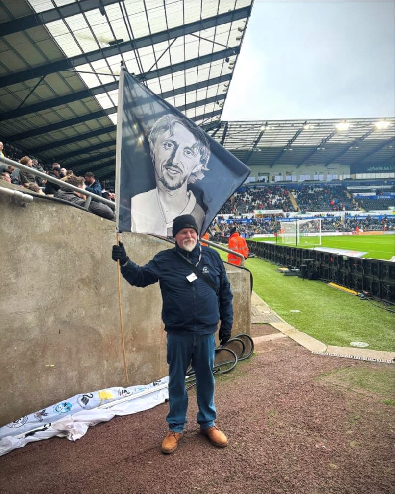 A crew member holding a tribute flag pitchside